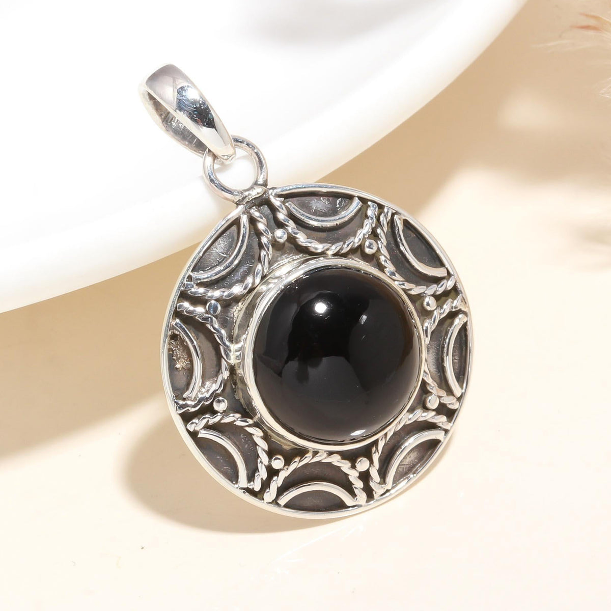 A round black onyx gemstone pendant set in a sterling silver mounting with intricate vintage-style detailing.