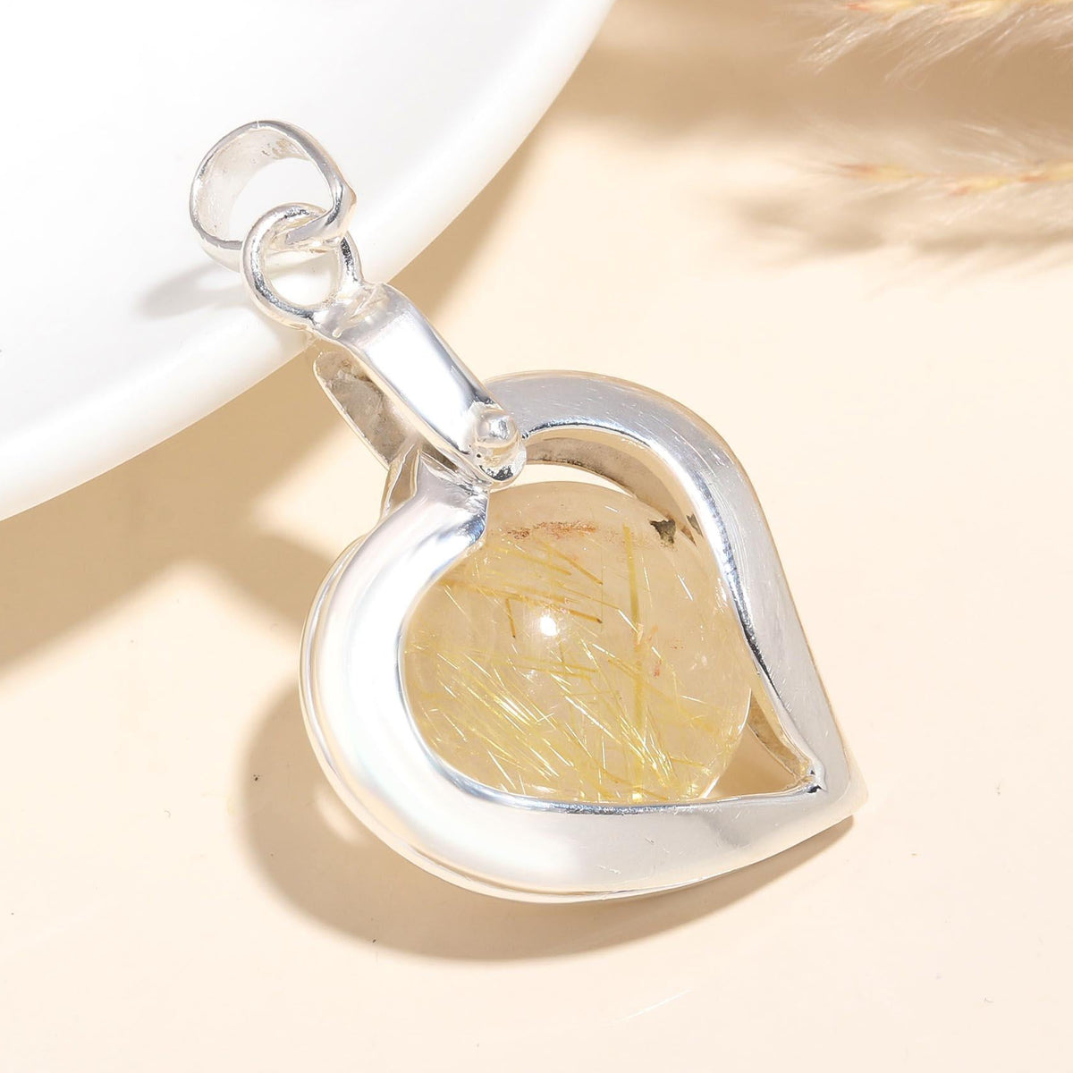 A heart-shaped 925 sterling silver pendant containing a rutilated quartz gemstone, displayed against a neutral background.