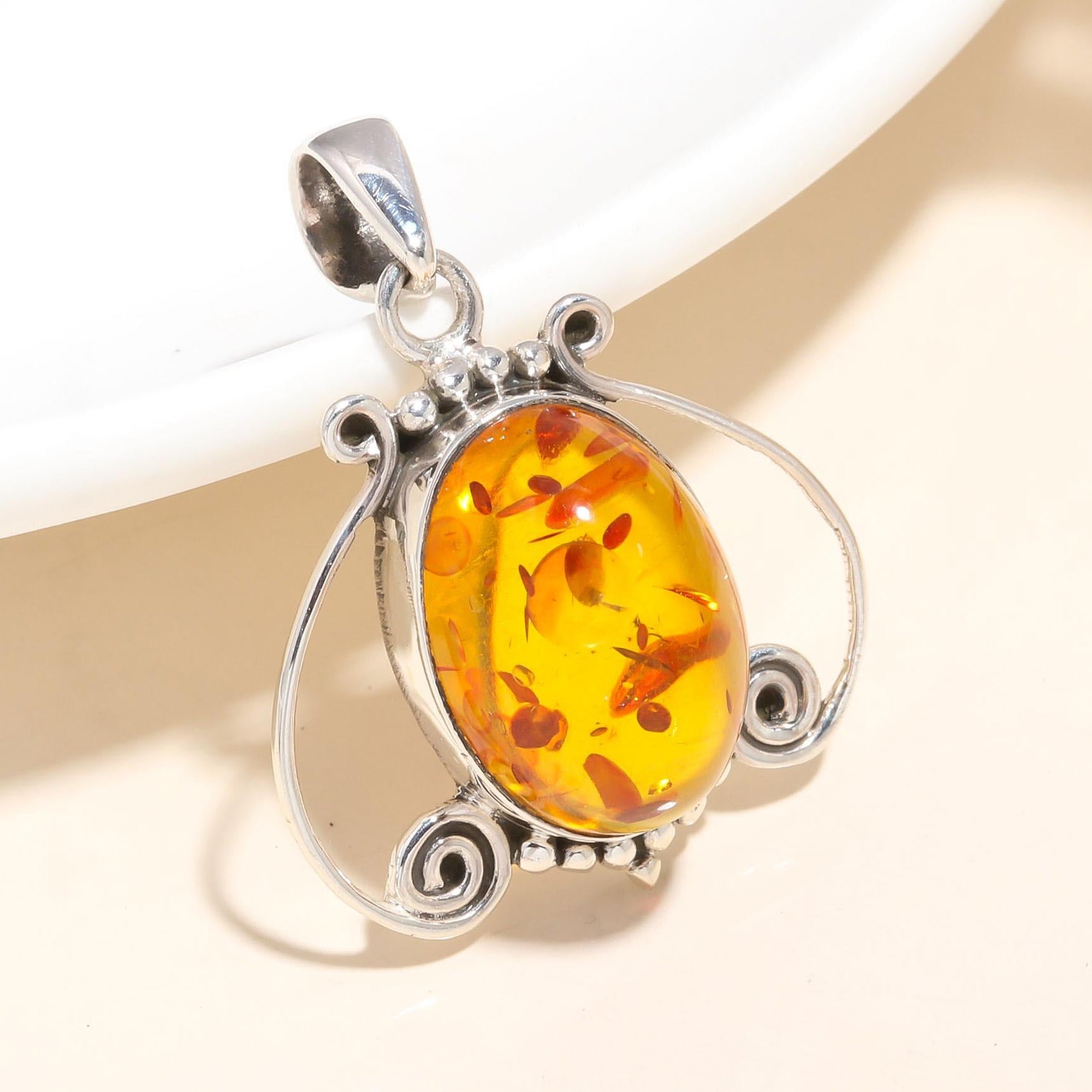A vintage-style sterling silver pendant with natural Baltic amber, presented on a white dish.