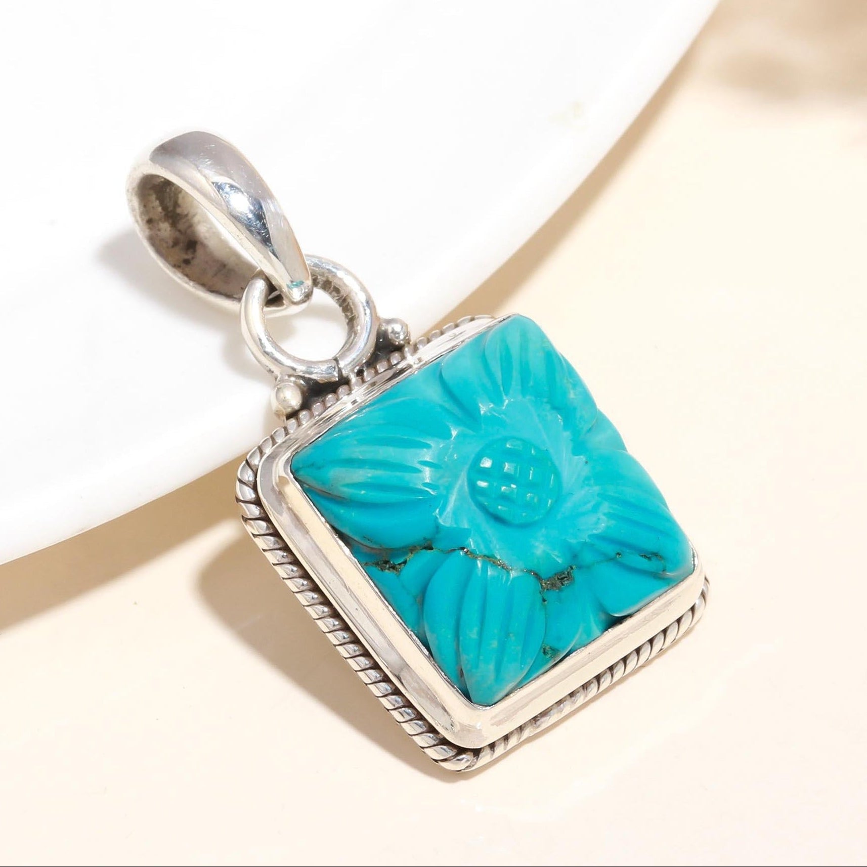 A sterling silver floral-inspired design pendant with a carved turquoise gemstone, displayed against a neutral background.