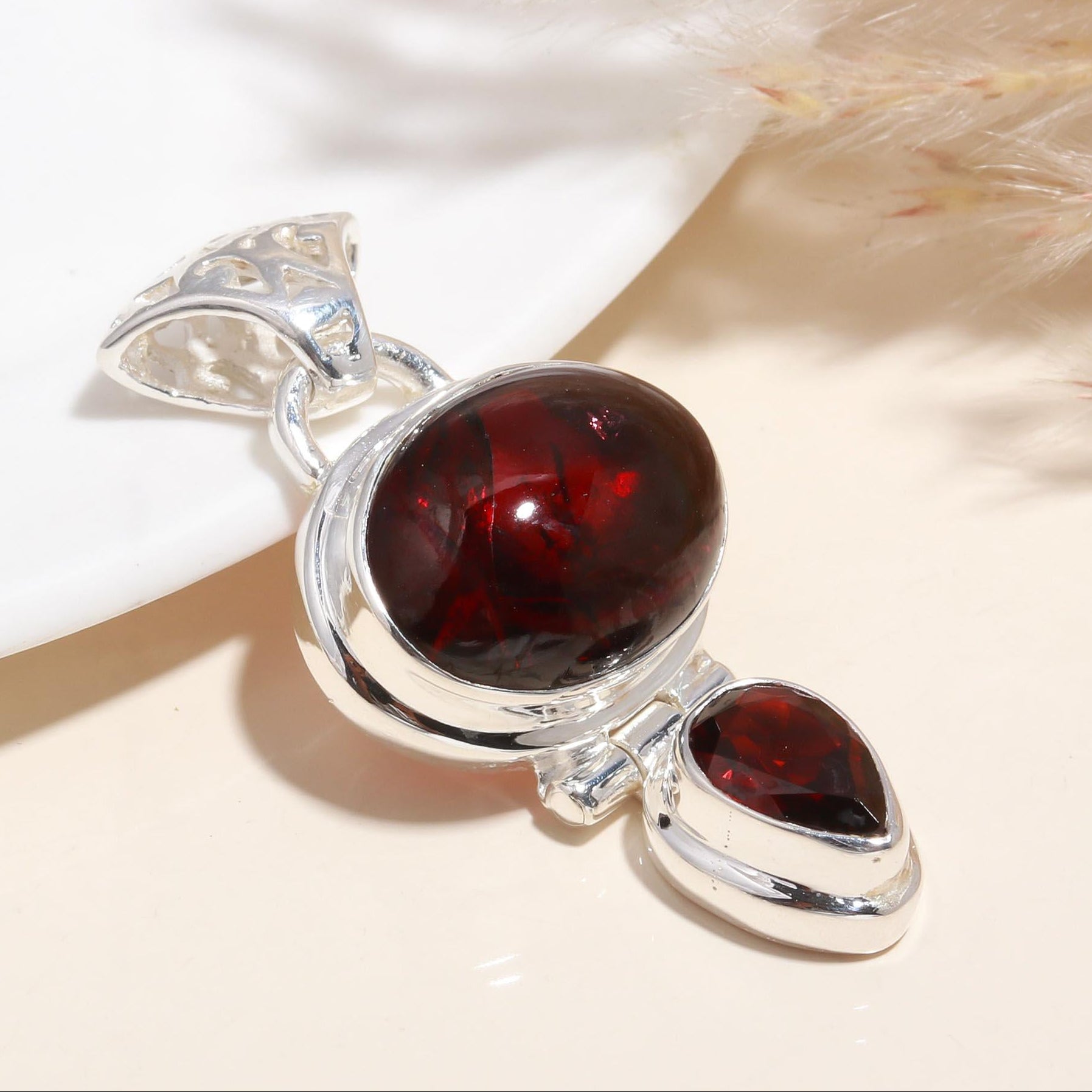 A sterling silver pendant featuring a large oval red garnet gemstone with smaller garnet stones in a handcrafted setting.