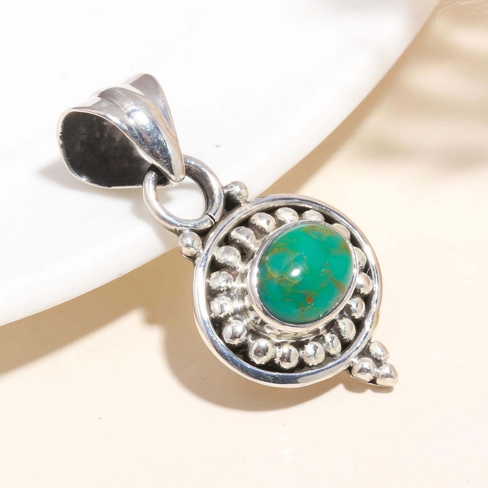 A 925 Sterling Silver pendant with a central turquoise gemstone, surrounded by intricate silver detailing, displayed against a neutral background.