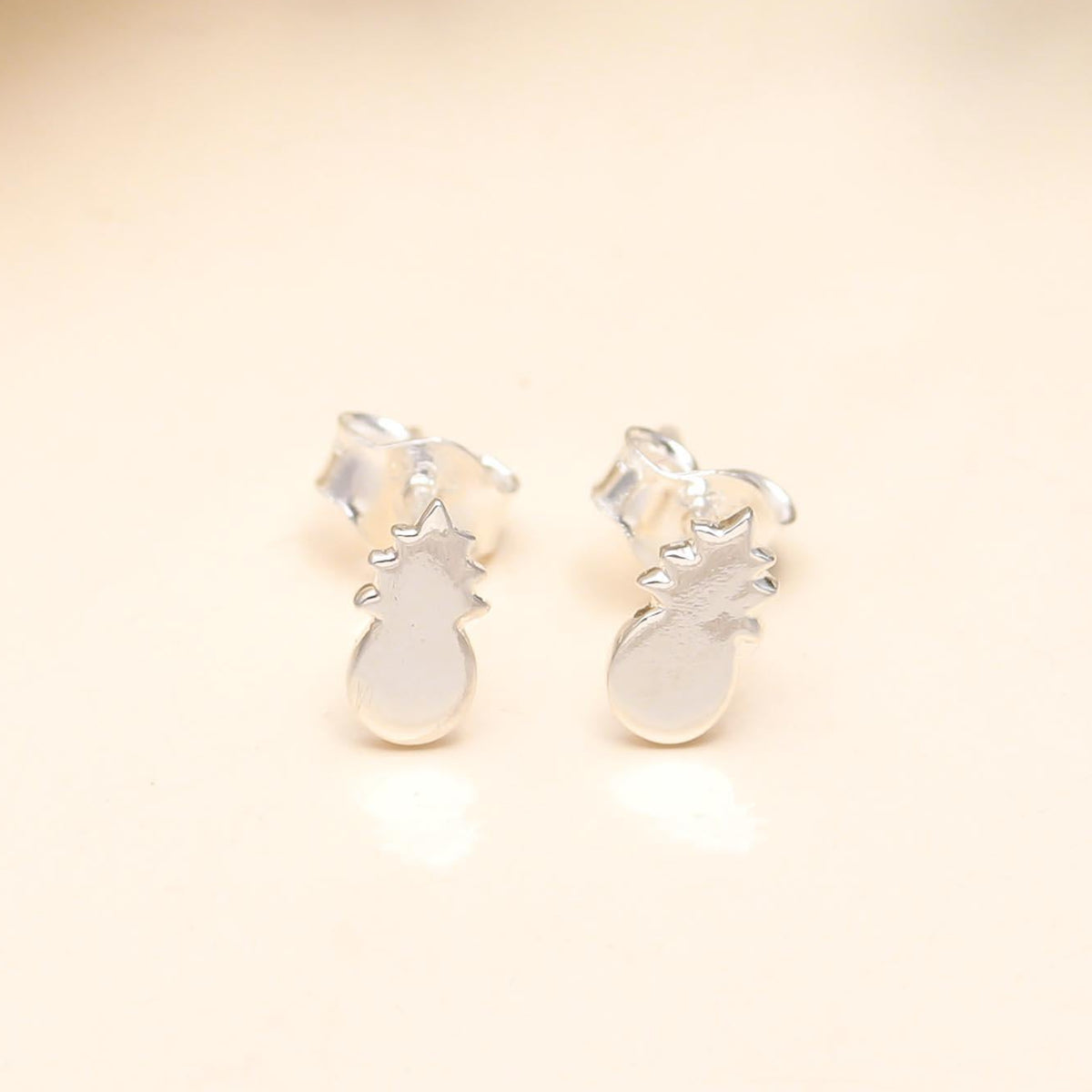 Silver pineapple-shaped earrings on a beige background