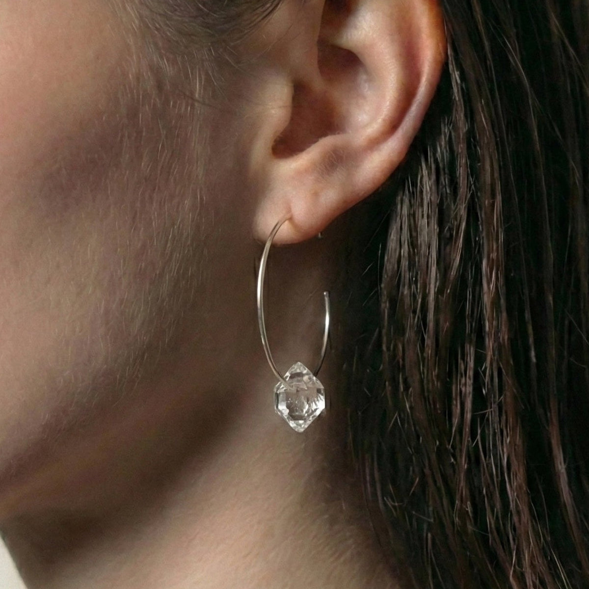 Close-up of a person wearing a silver hoop earring with a clear gemstone.