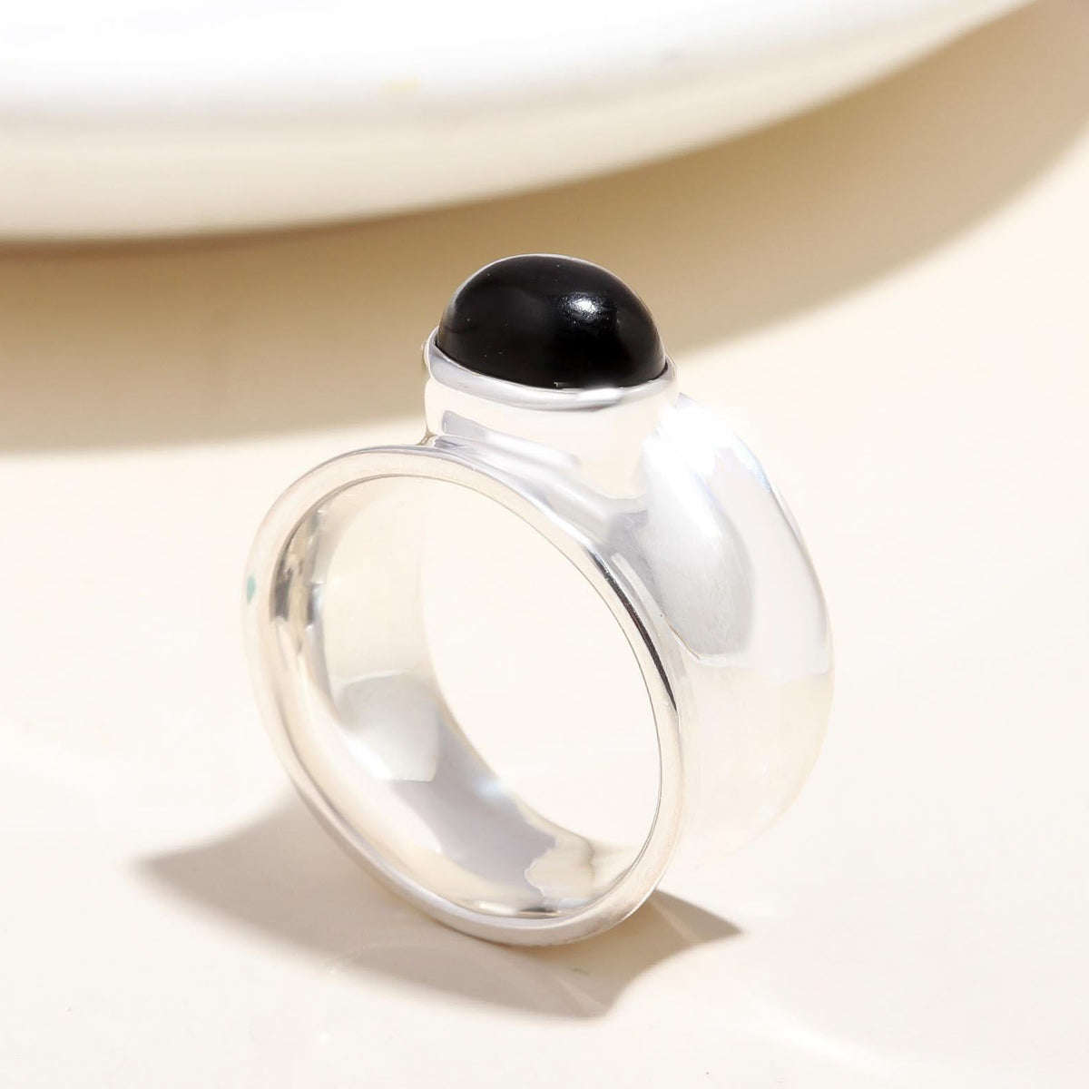 Silver ring with a black gemstone on a beige background