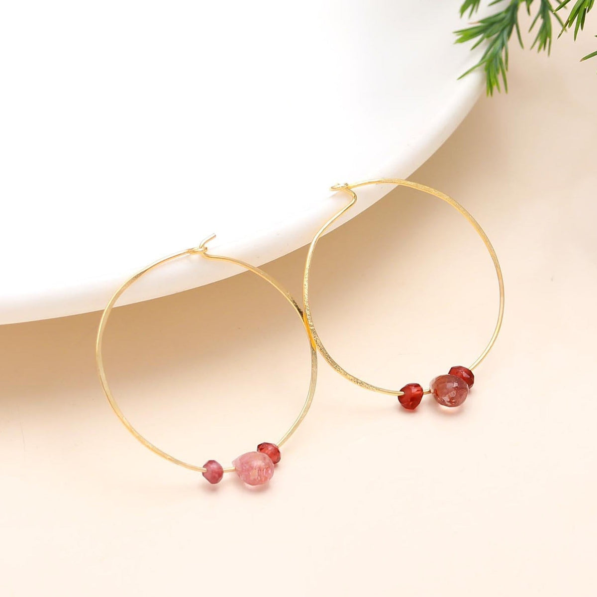 Gold hoop earrings with red beads on a beige background
